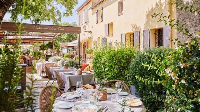 Charming outdoor restaurant patio with arranged tables, surrounded by greenery and a rustic building.